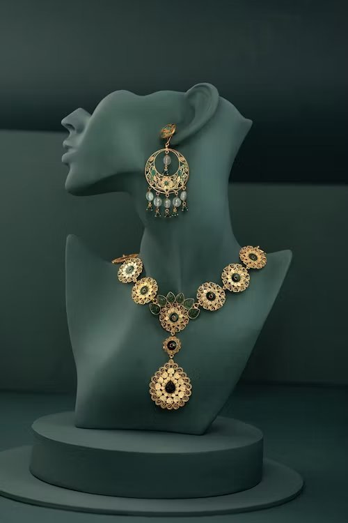 Gold kundan-style necklace and drop earrings displayed on a bust, editorial studio photography